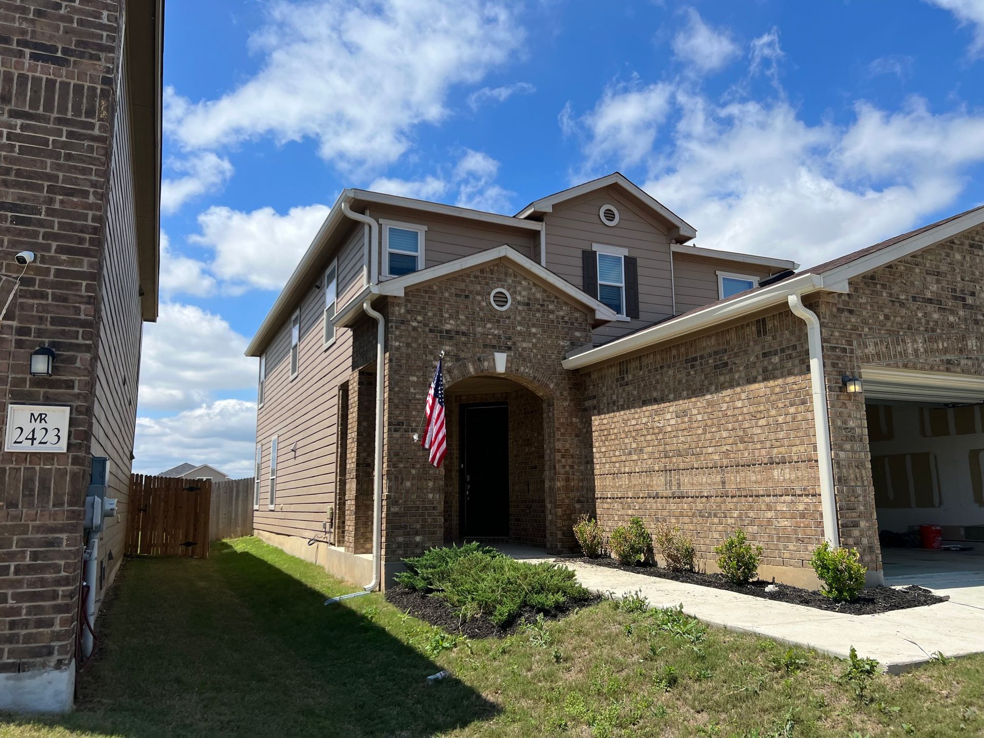 Two-story brick house with a front porch, an American flag, and a blue sky.