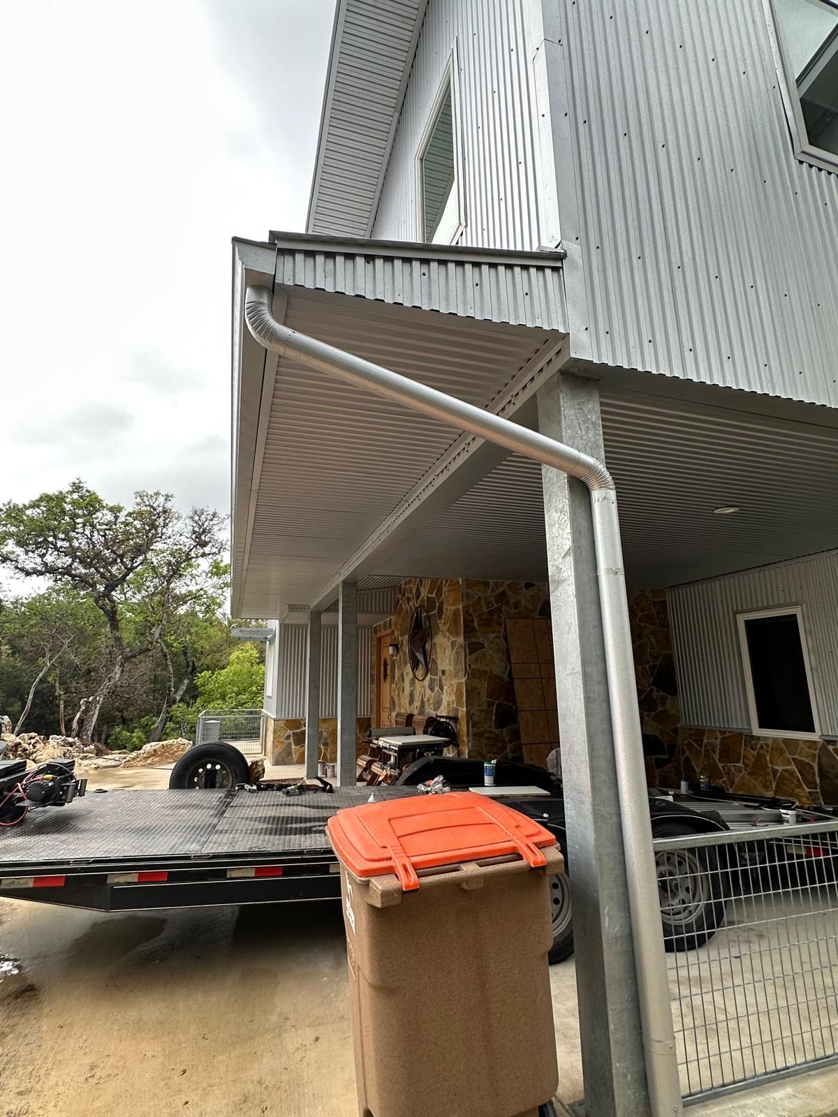 A building with metal siding and a covered porch with a trash can in the foreground.
