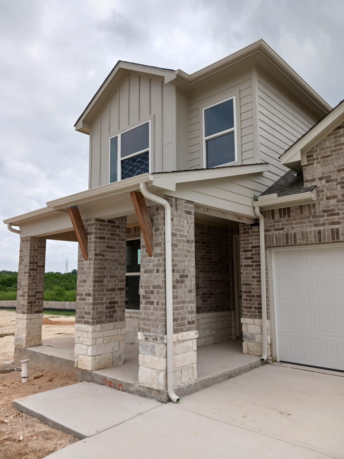 Two-story house exterior with brick and stone accents, covered porch, and a garage. Cloudy sky.