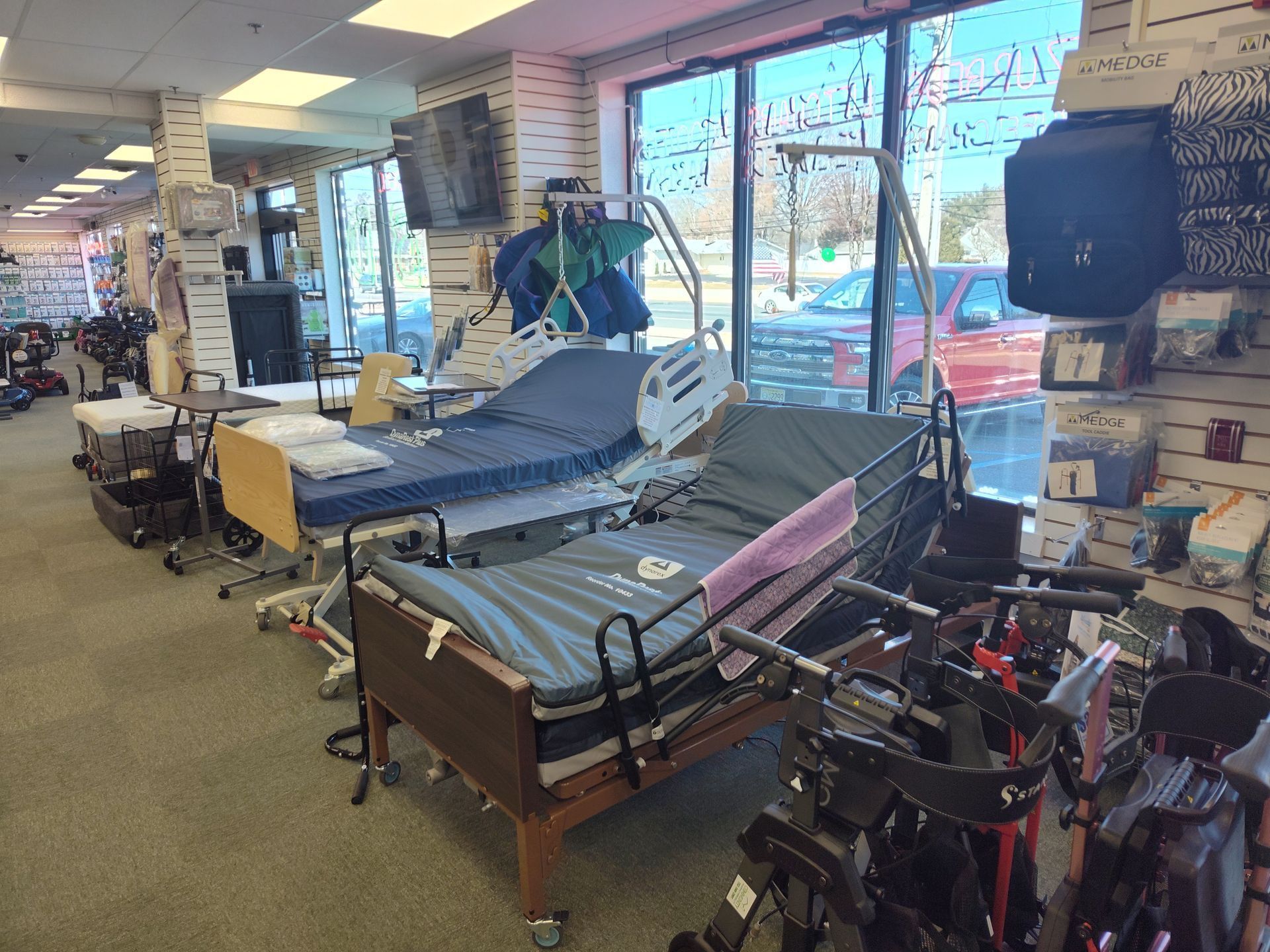 Inside a medical supply store, adjustable beds and mobility aids are on display near a large window.