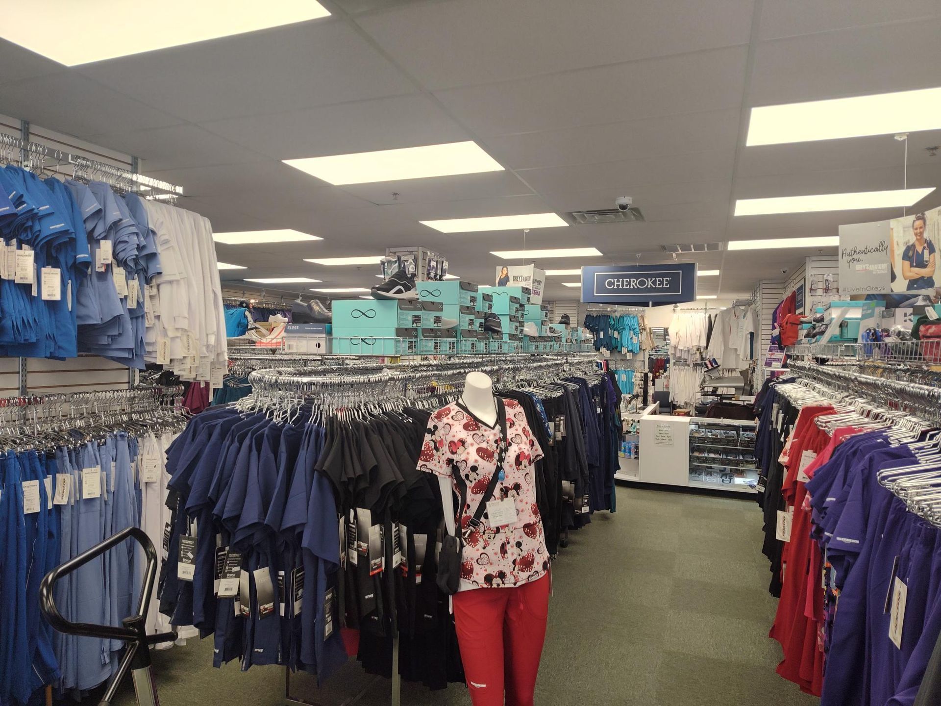 Clothing store interior with racks of scrubs in various colors; mannequin wearing a floral scrub top.
