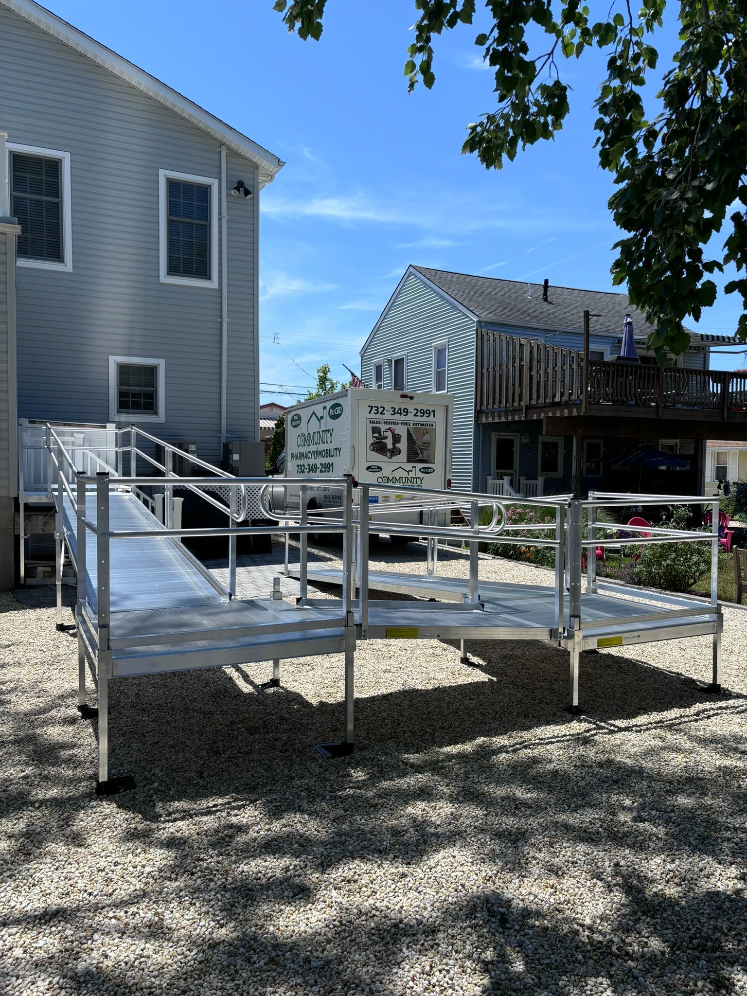Aluminum wheelchair ramp leading to a light blue building, set on small stones. Bright sunny day.