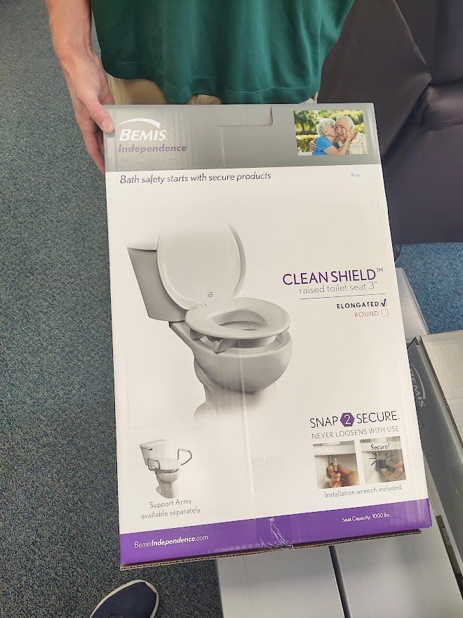 Person holding a box for a Clean Shield toilet seat. The box is gray with a photo of the product.