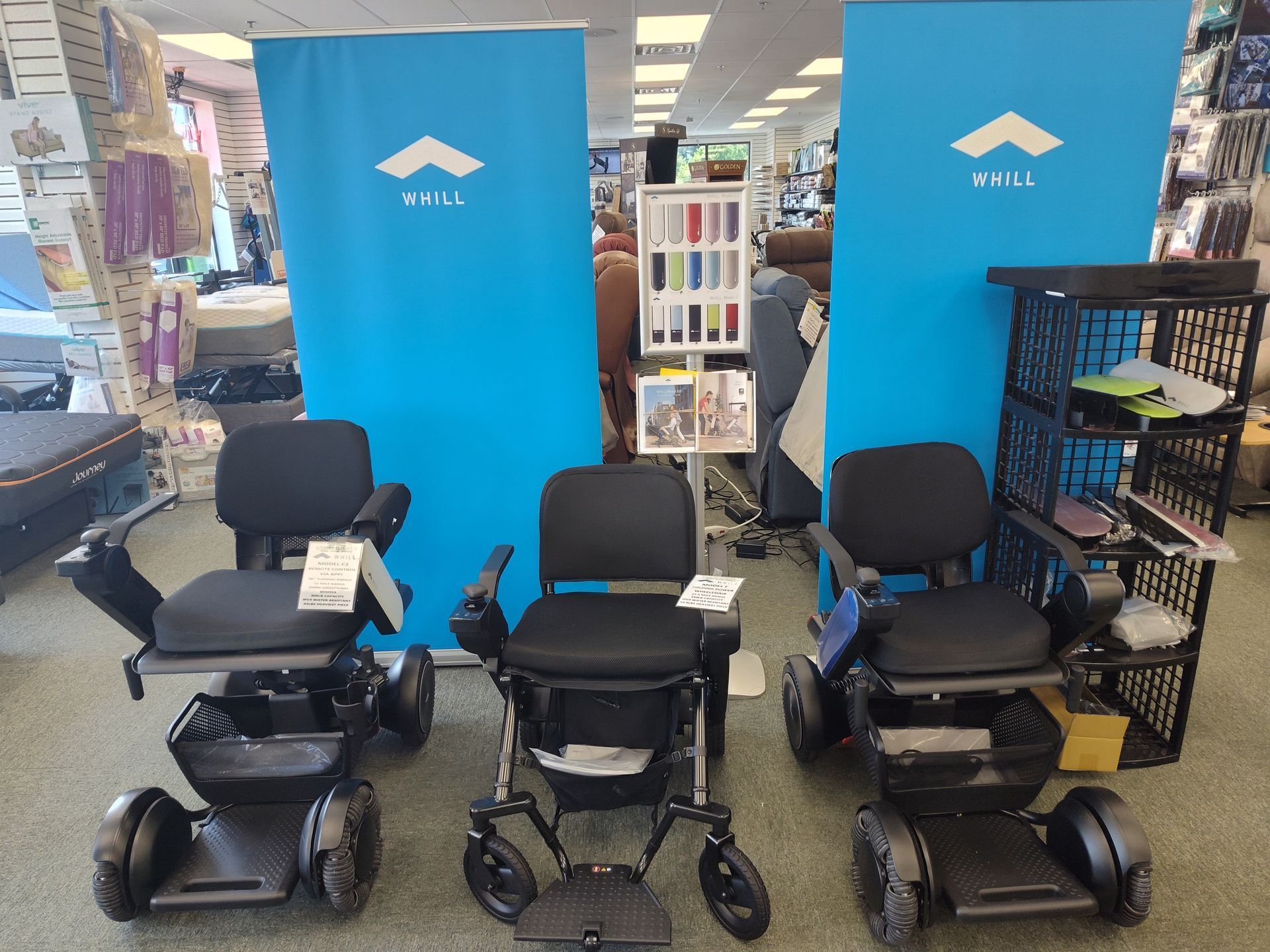 Three black power wheelchairs displayed in a store with blue banners.