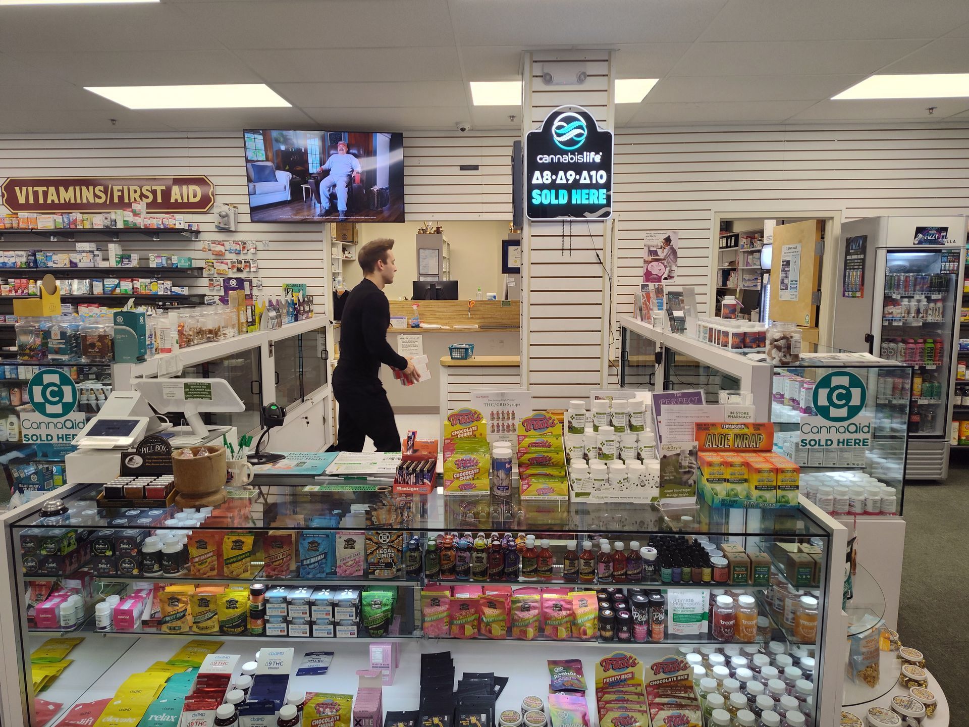 Interior of a pharmacy with shelves of products, a counter, and a person walking.