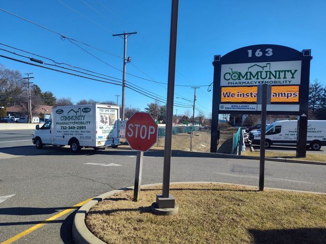 A white van with Community Pharmacy Services logo parked in front of a shopping center sign.