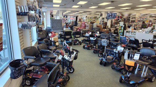 Shop interior filled with mobility scooters and accessories. White walls, bright lighting, many products on display.