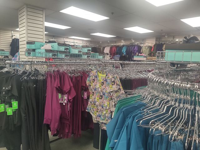 Clothing store interior with racks of scrubs in various colors and styles.