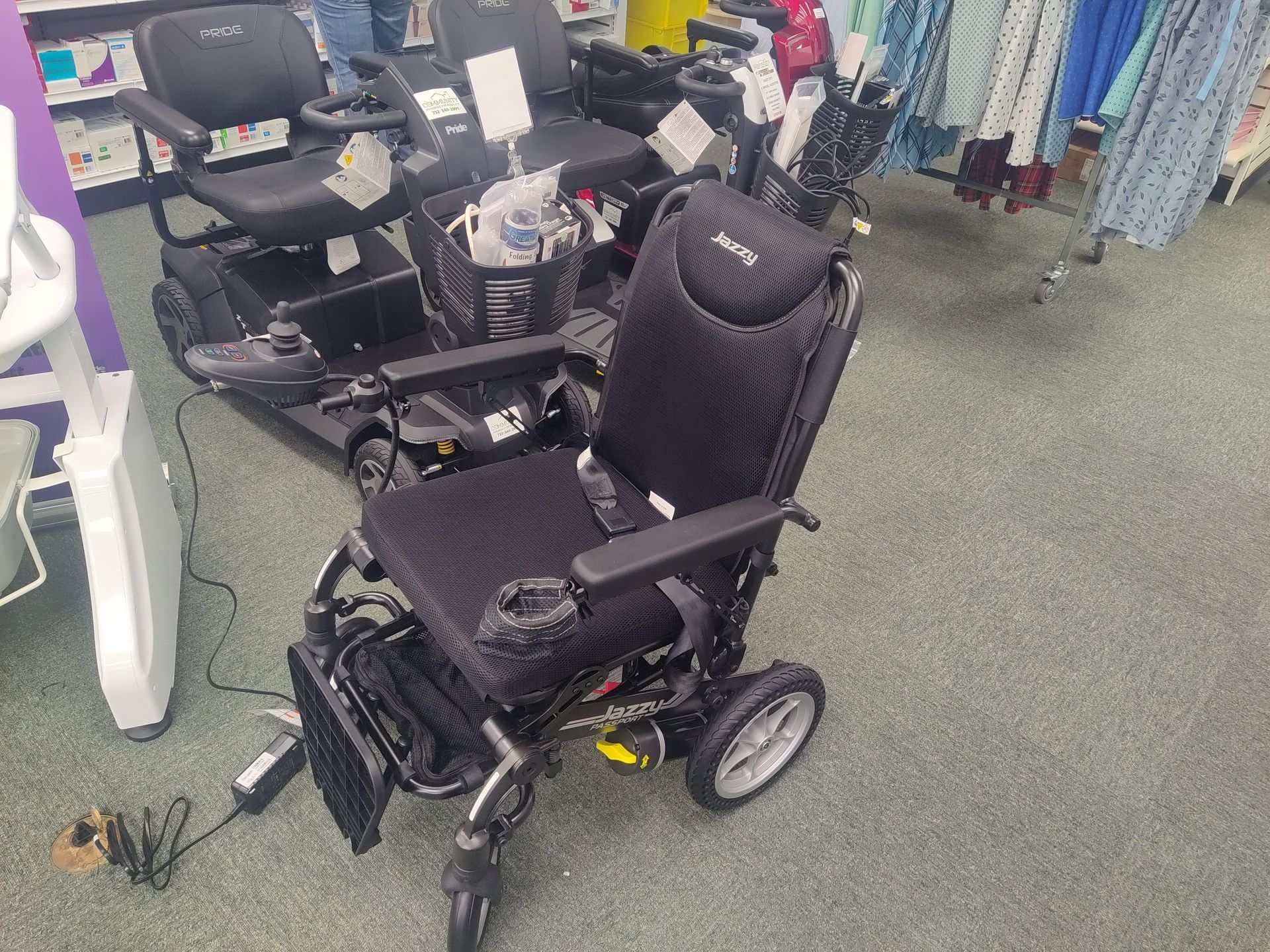 Black electric wheelchair in a store, with other mobility devices in the background.