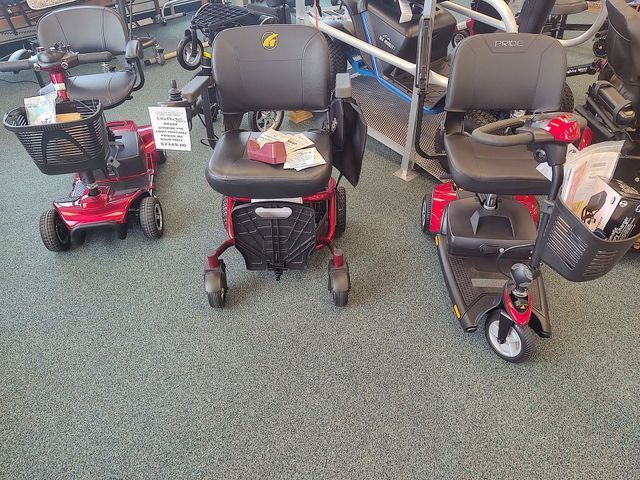 Three red and black mobility scooters on display in a store, with baskets and seats.