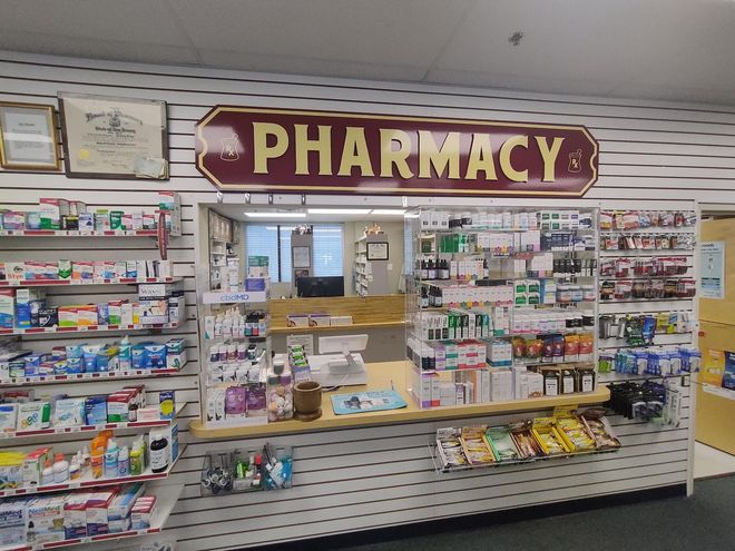 Pharmacy counter with "PHARMACY" sign. Shelves hold medications.