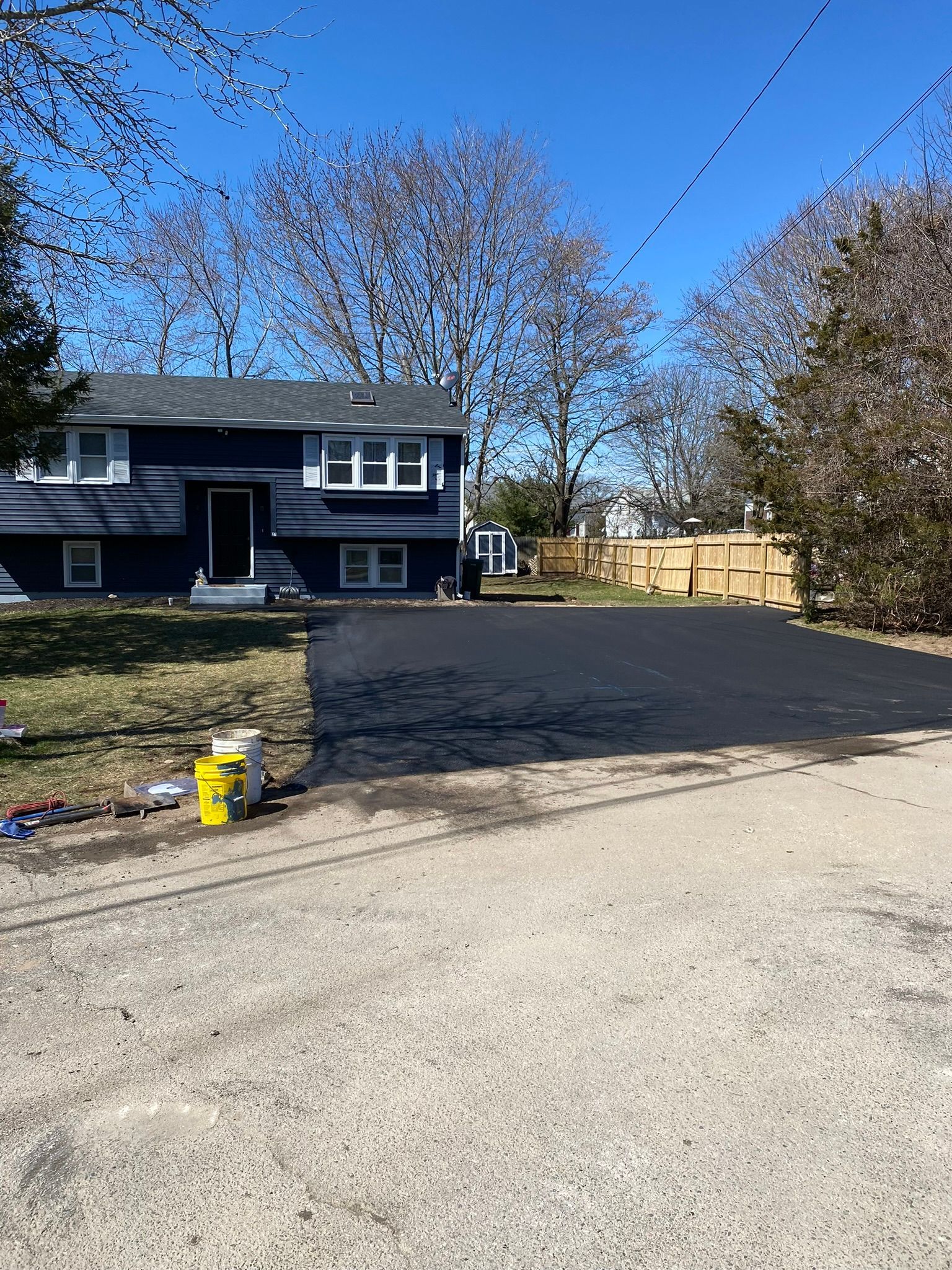 Dark blue house with a newly paved black driveway, sunny day.