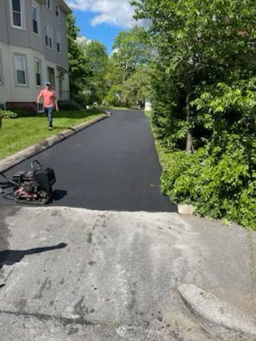 Freshly paved asphalt driveway. A man walks away in the background.  A vibrating compactor sits on the left.