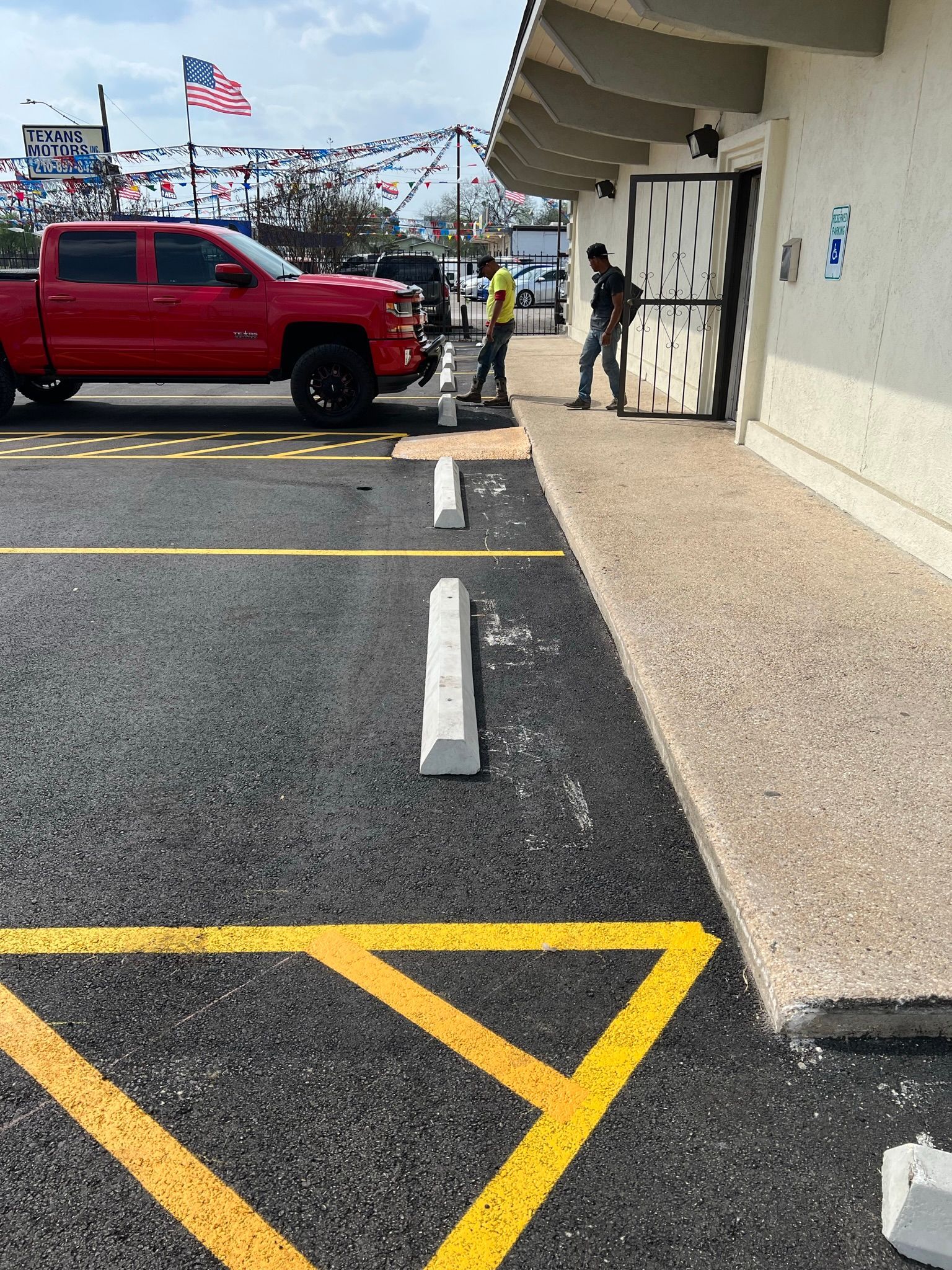 Workers installing a concrete parking barrier at a commercial building next to a red pickup truck.