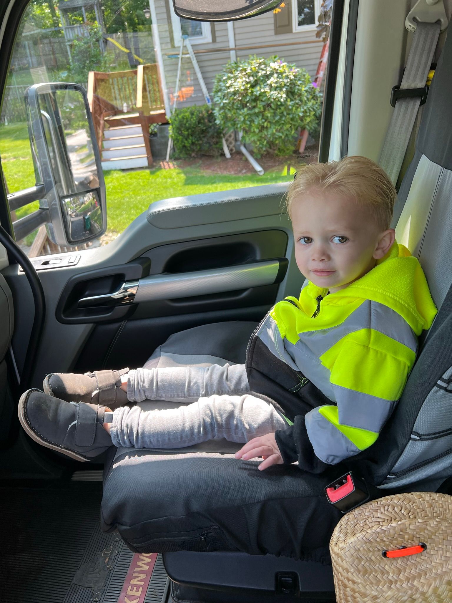 Young child in high-vis jacket sits in a truck cab, looking forward.  Sunlight streams through the window.
