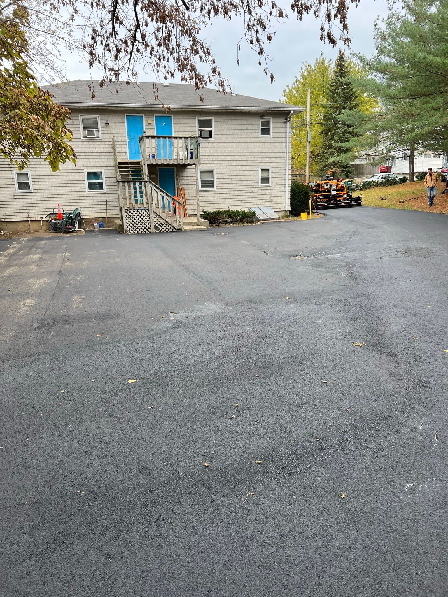 Gray two-story apartment building with blue doors; asphalt parking lot in front.