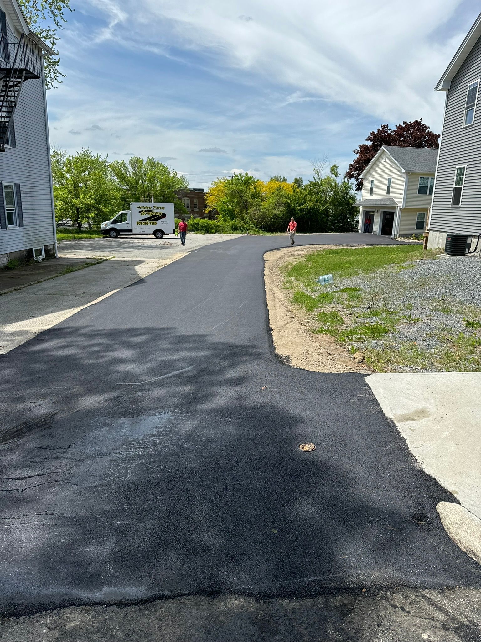 New asphalt road between two buildings with a moving truck and workers in the distance.