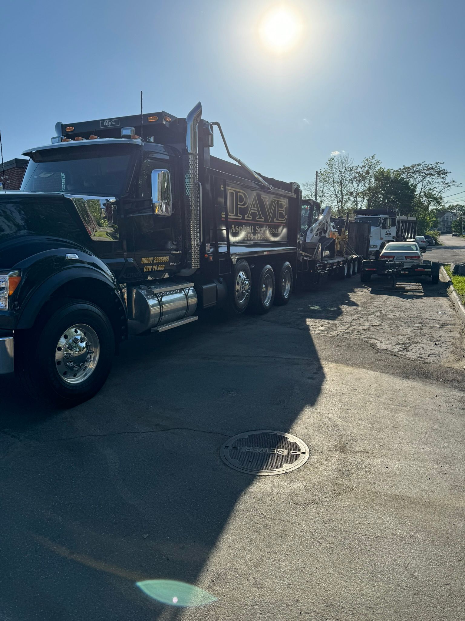 Black semi-truck parked on pavement in bright sunlight.