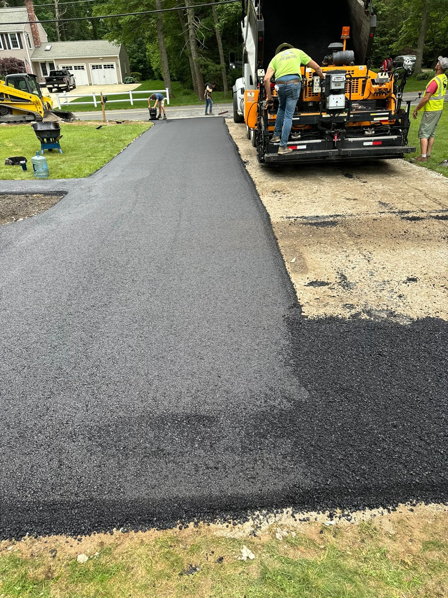 Asphalt paving a driveway; workers operate machinery, spreading dark material on the surface.