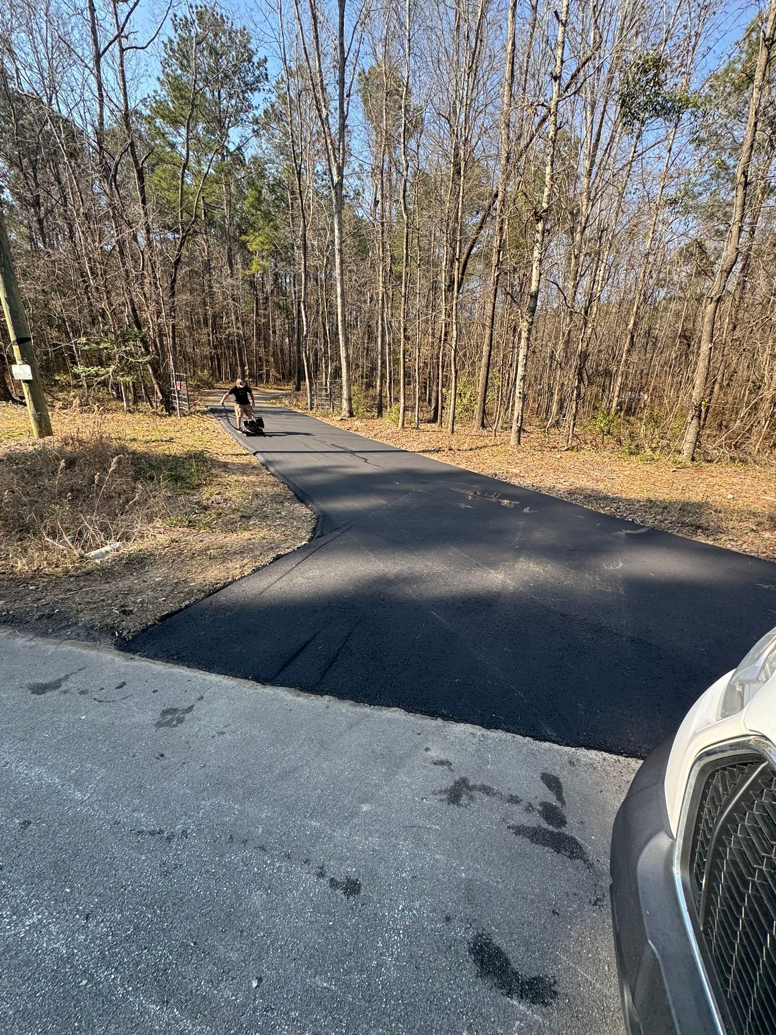 Asphalt path through woods, person on bike, car parked.