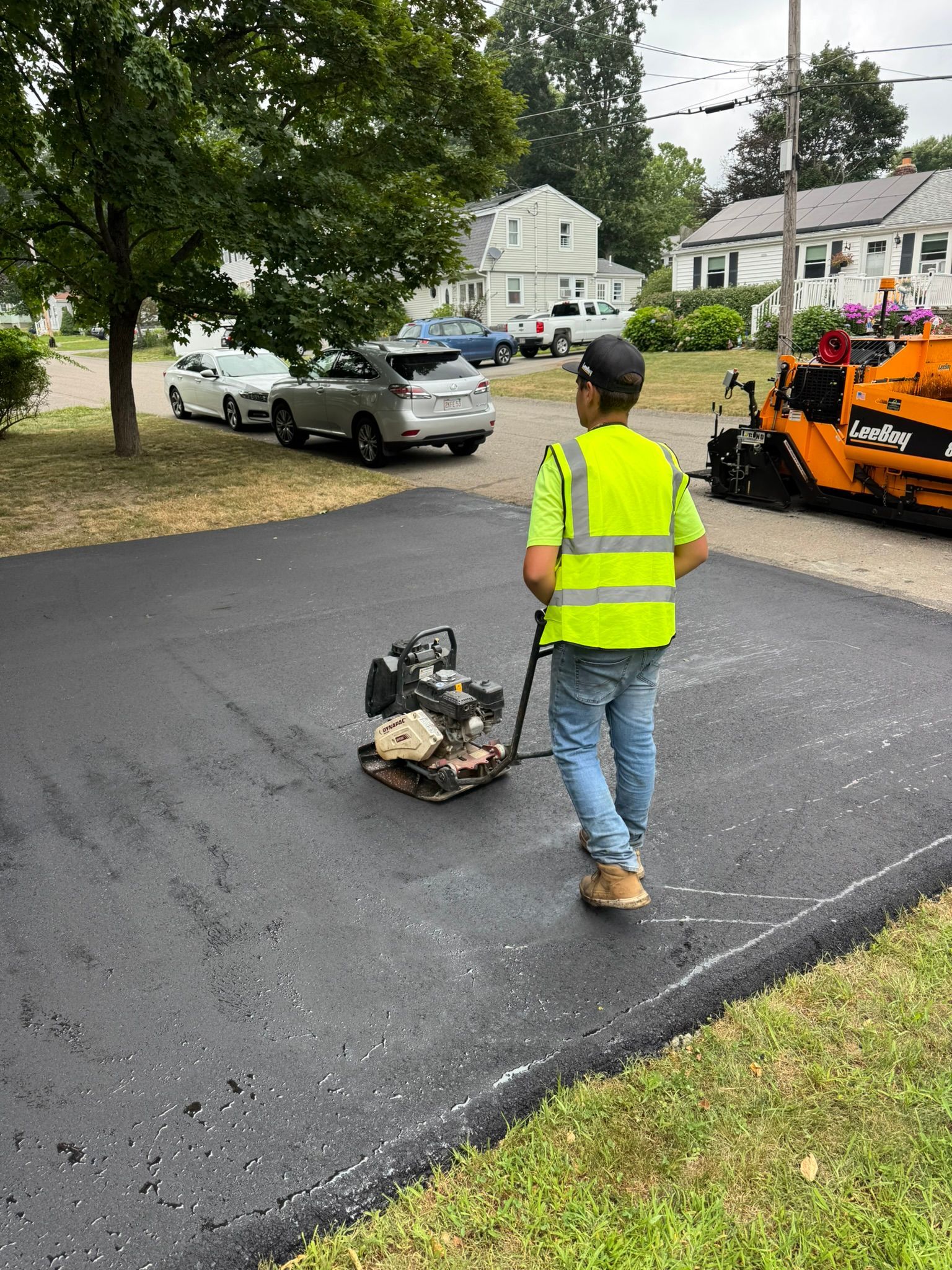 Worker in neon vest uses a plate compactor on freshly paved asphalt.