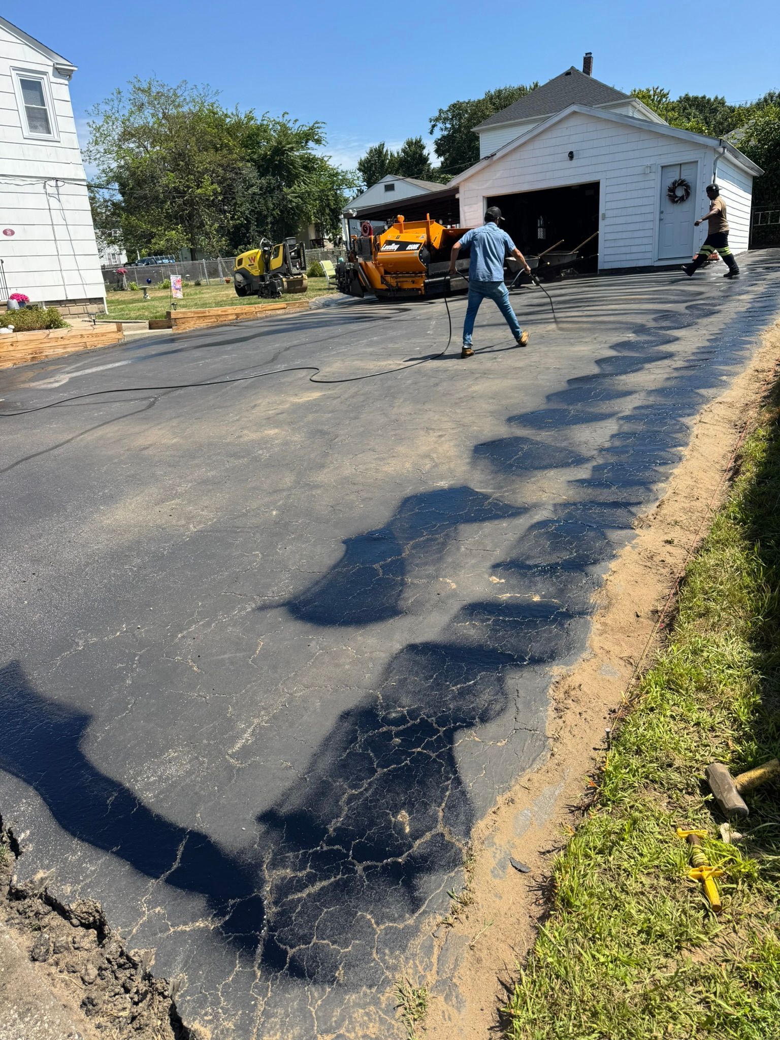 Asphalt driveway being repaved with a man and machinery working on a sunny day.