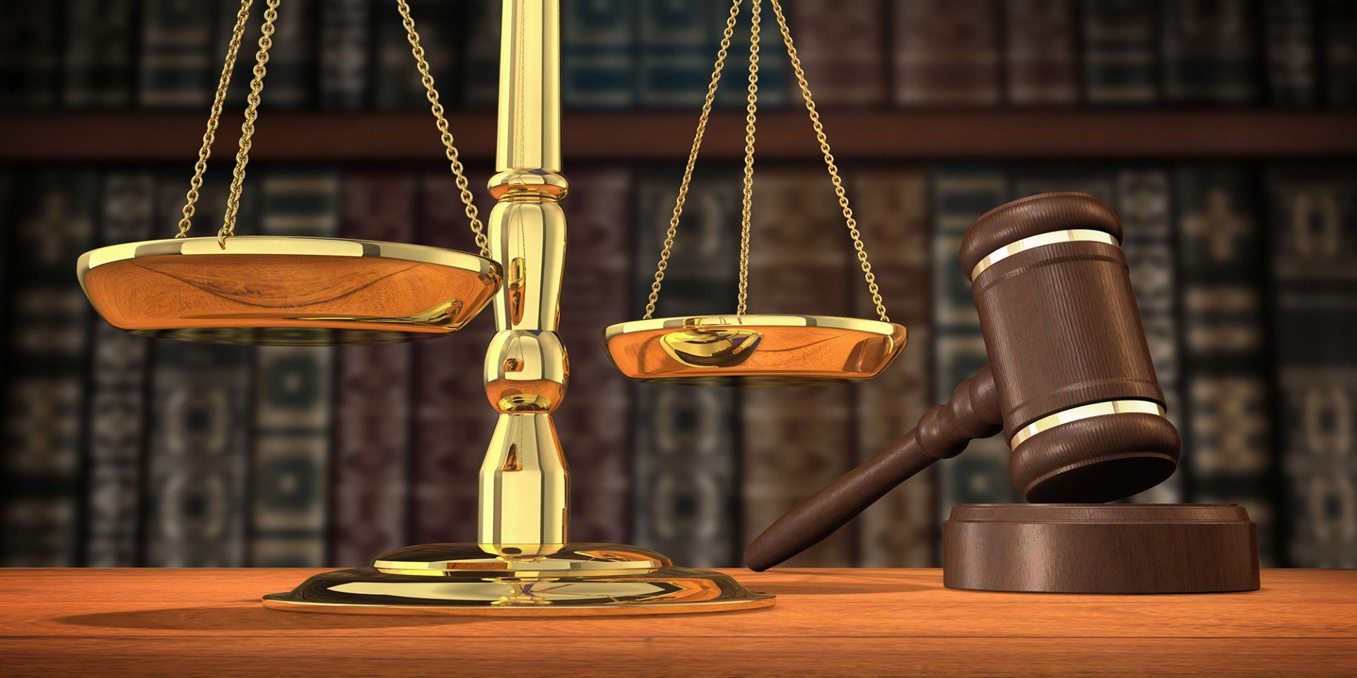 A scale of justice and a judge 's gavel are on a wooden table in front of a bookshelf.
