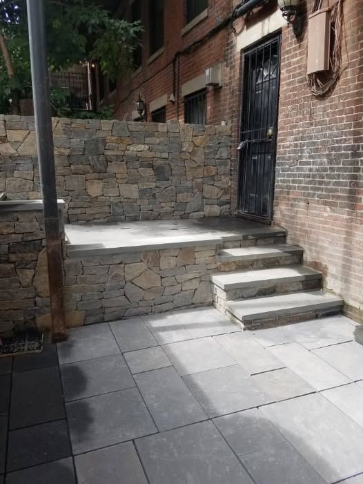 a stone wall surrounds a patio with stairs leading up to a door