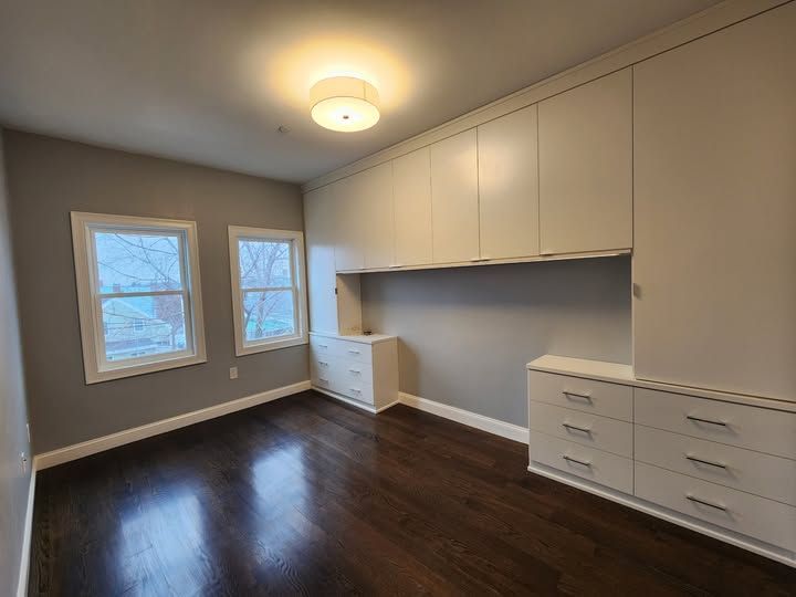 an empty room with hardwood floors and white cabinets