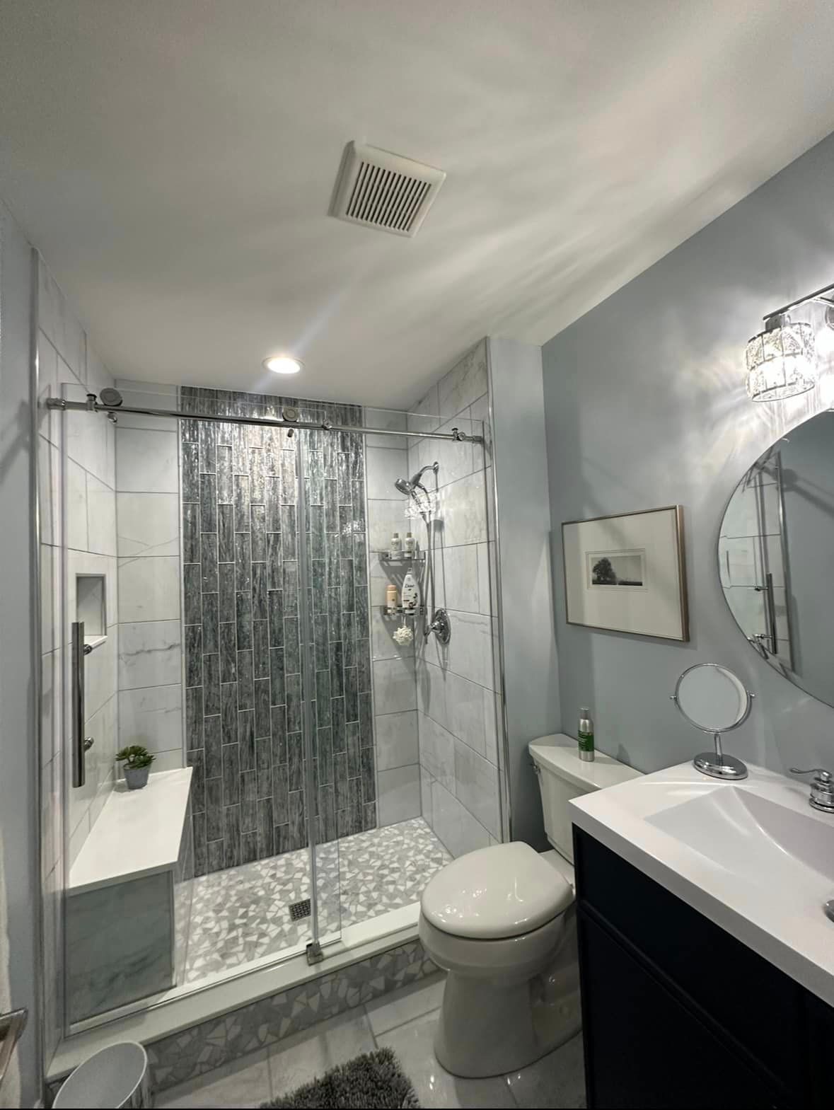 A bathroom with a toilet, sink, shower and mirror.