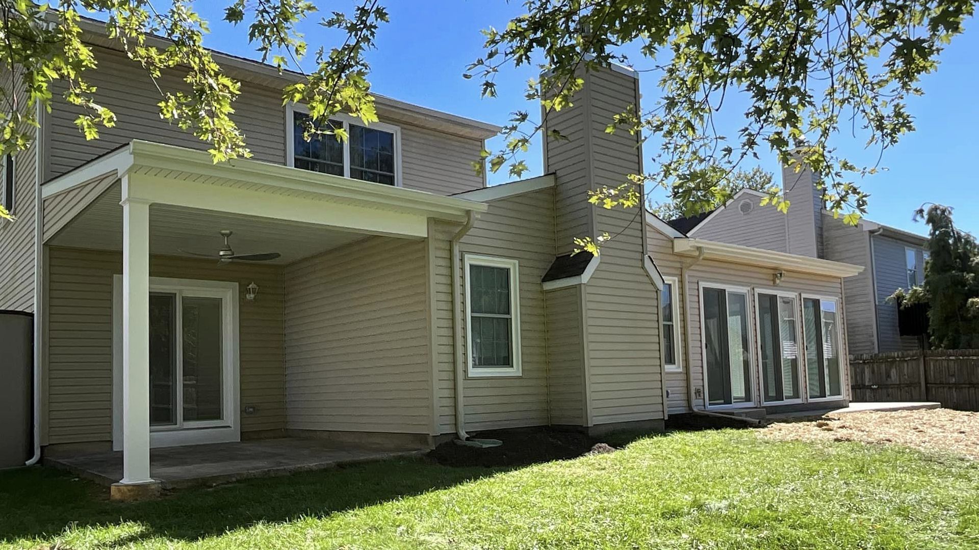 The back of a house with a covered patio and a lot of windows.