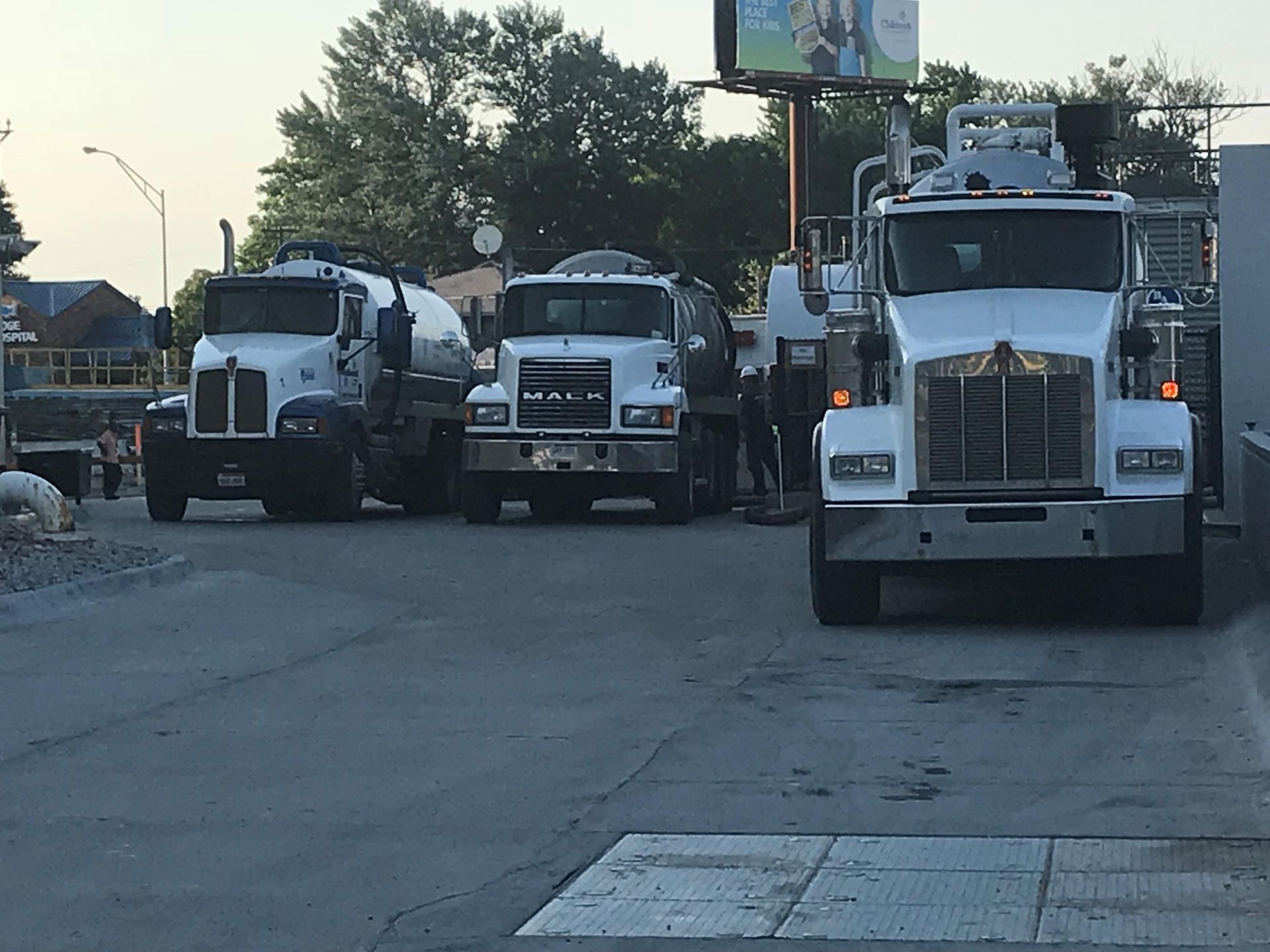 Three white semi trucks parked side by side in a lot at dusk