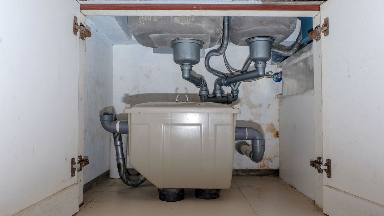 Under-sink cabinet with exposed plumbing and a compact water heater unit inside