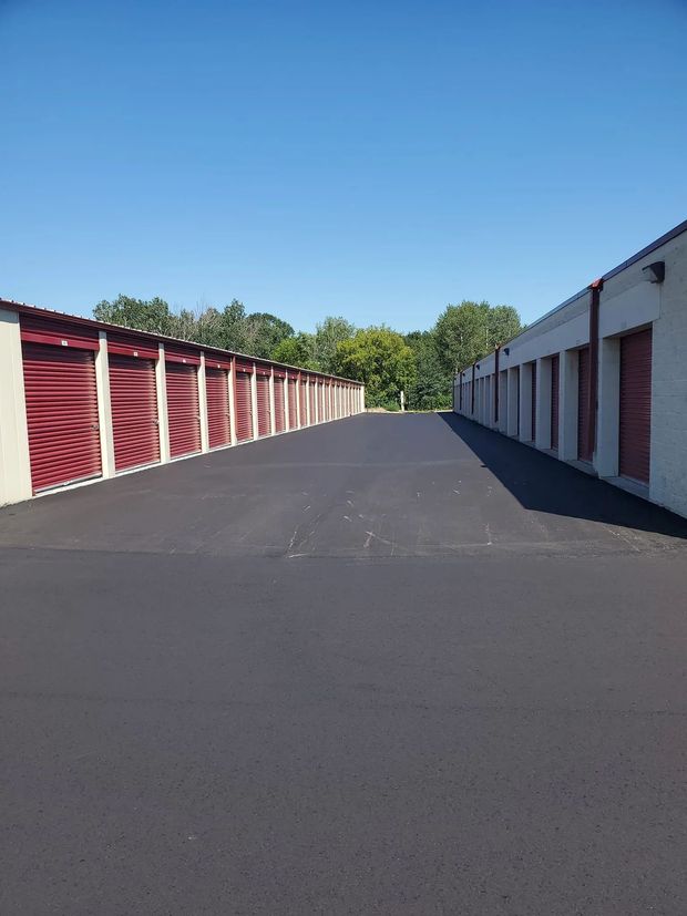 Rows of storage units with red doors and asphalt drive, under a blue sky.