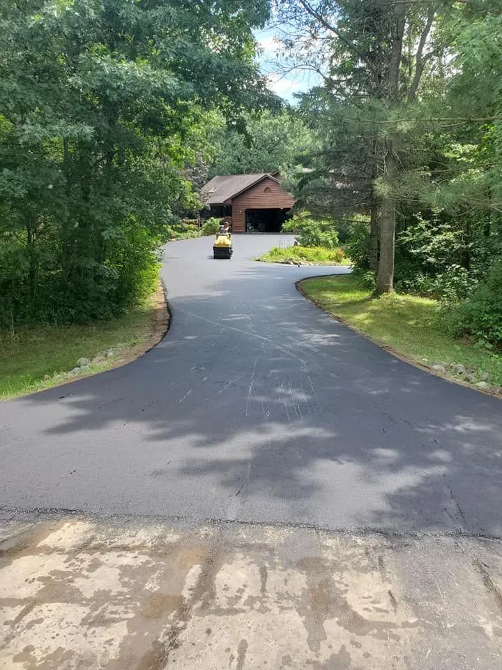 Newly paved asphalt driveway leading to a house with trees.