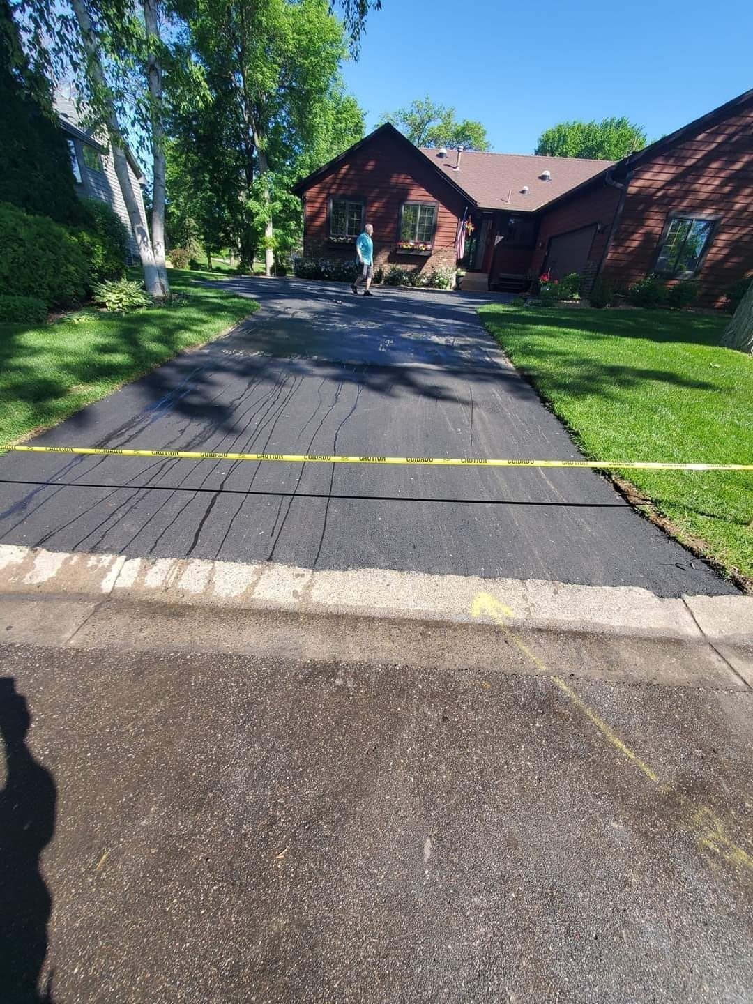 Asphalt driveway with cracks, caution tape, leading to a house, green lawn.