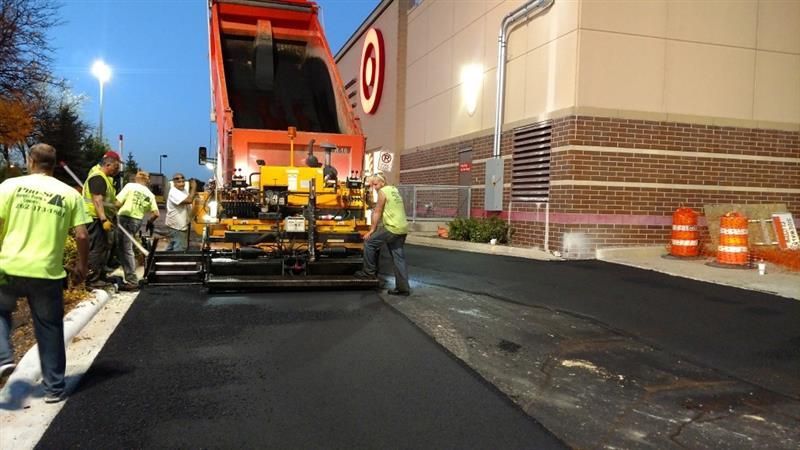 Asphalt paving at a Target store. Workers in safety vests guide paving machine.