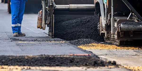A man is standing next to a machine that is paving a road.