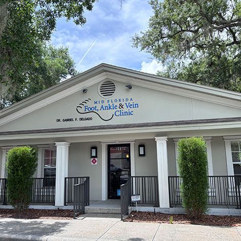 Front entrance of a white Foot, Ankle & Vein Clinic with columns and black railings under trees