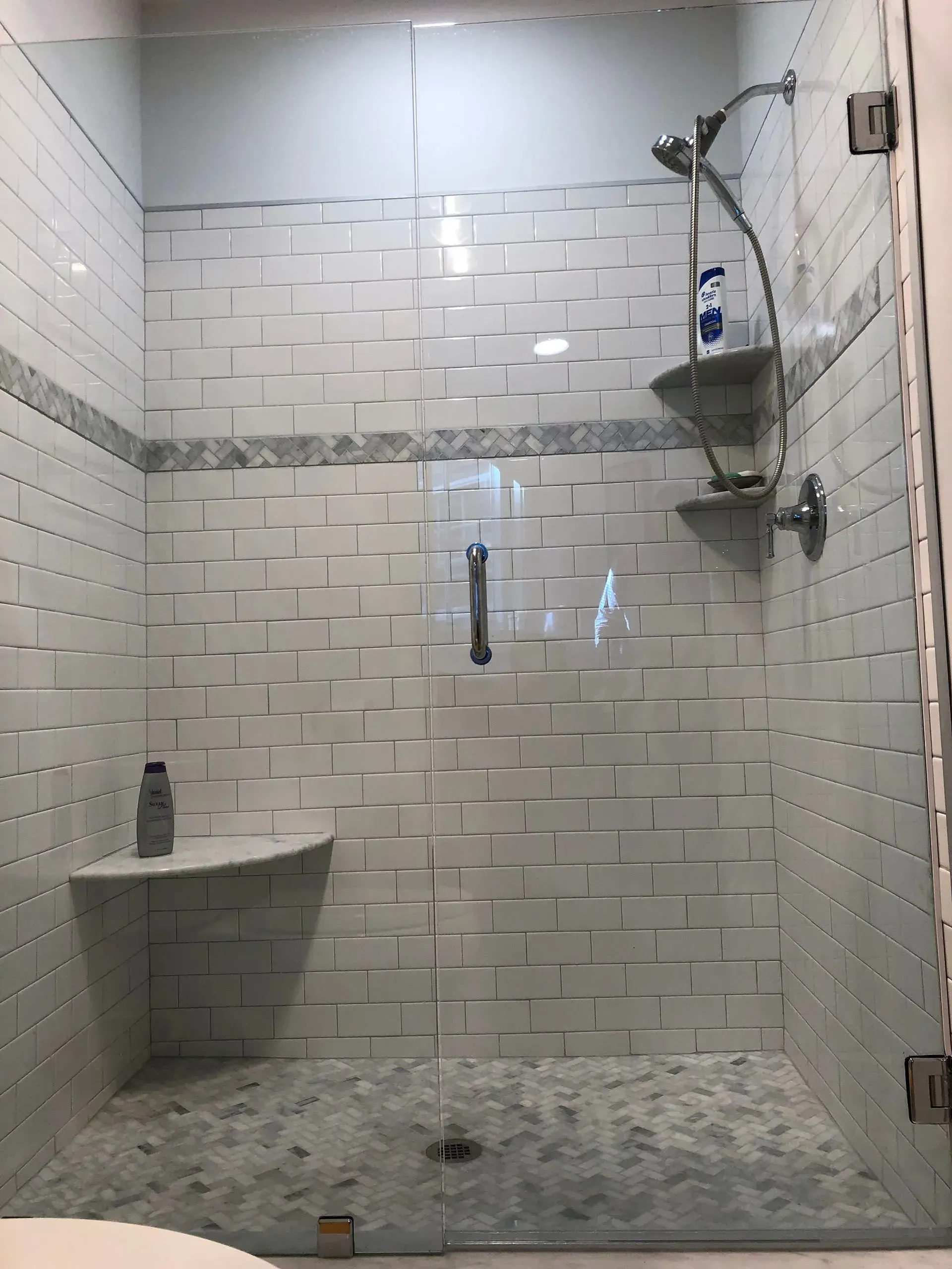 Shower with white textured tile walls, clear glass door, and pebble floor.
