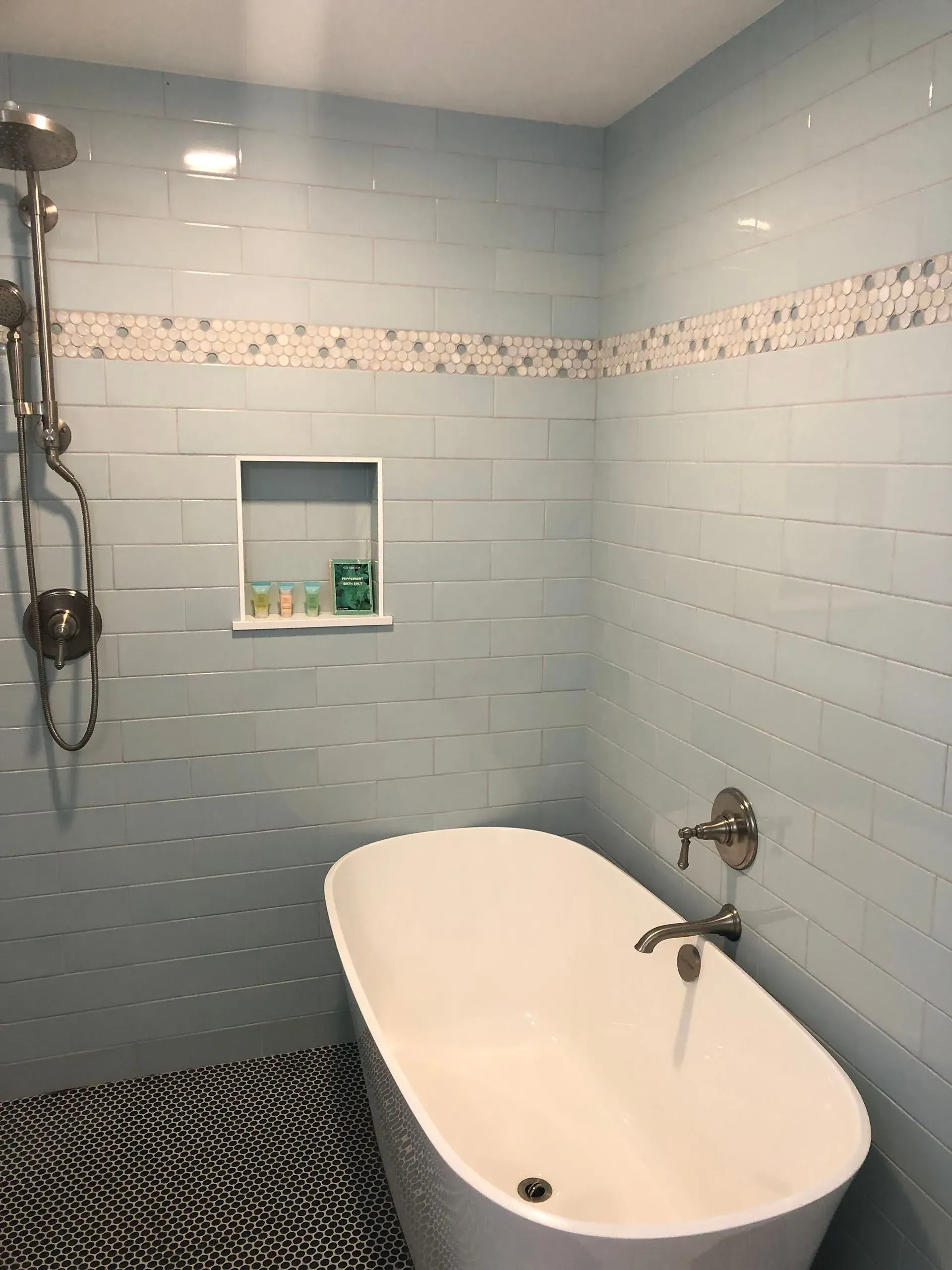 Bathroom with blue tile walls, white tub, silver showerhead, and black and white patterned floor.