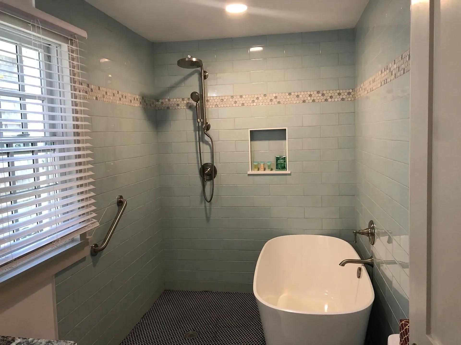 Bathroom with a blue tiled shower, a standalone tub, and a window with blinds.