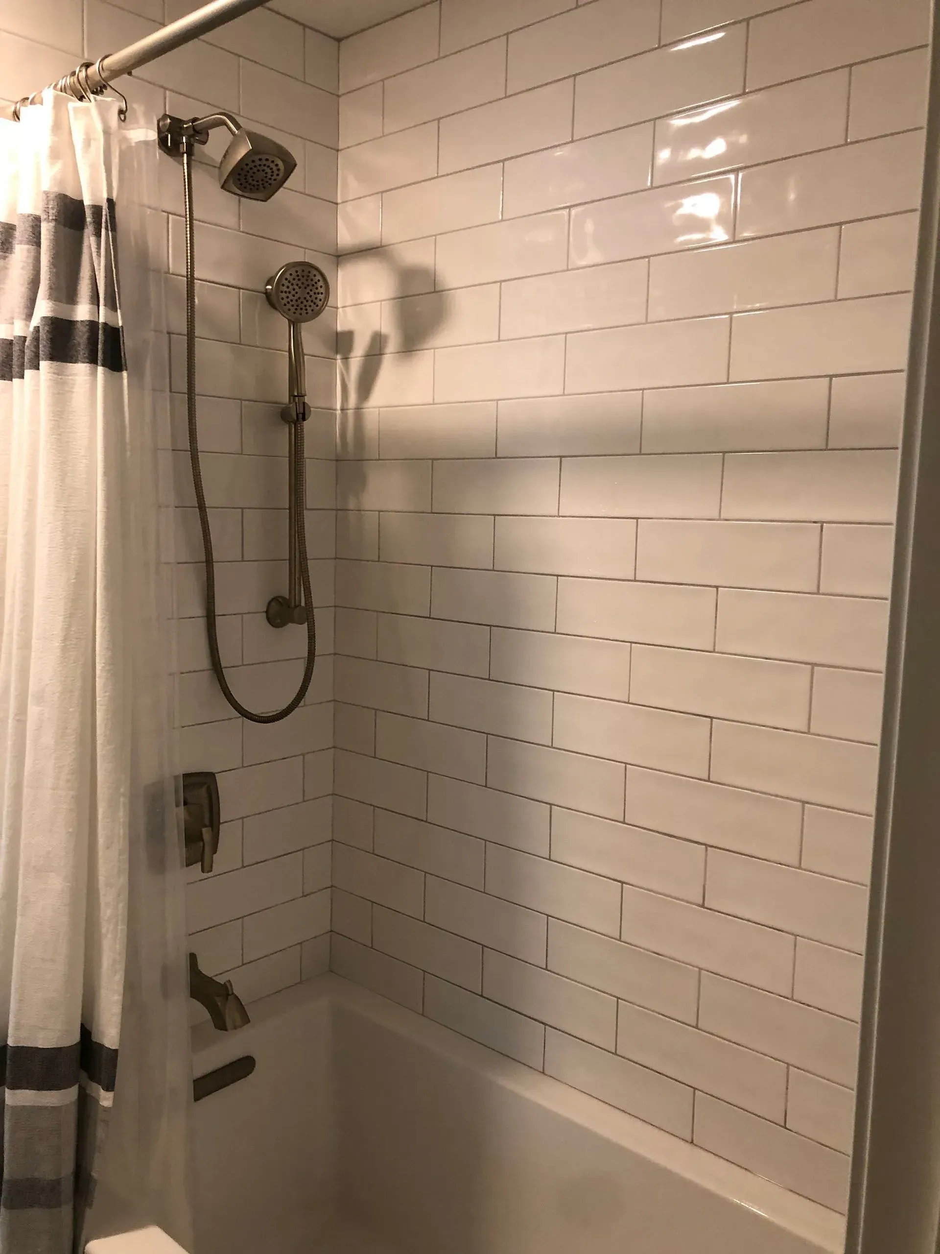 A modern white-tiled shower with showerhead, handheld shower, and bathtub.