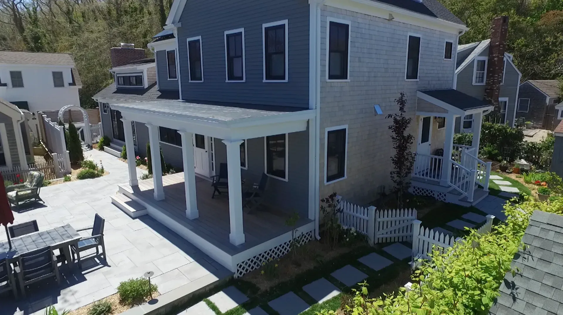 Two-story house with a porch. Gray siding, white trim, picket fence, outdoor seating.
