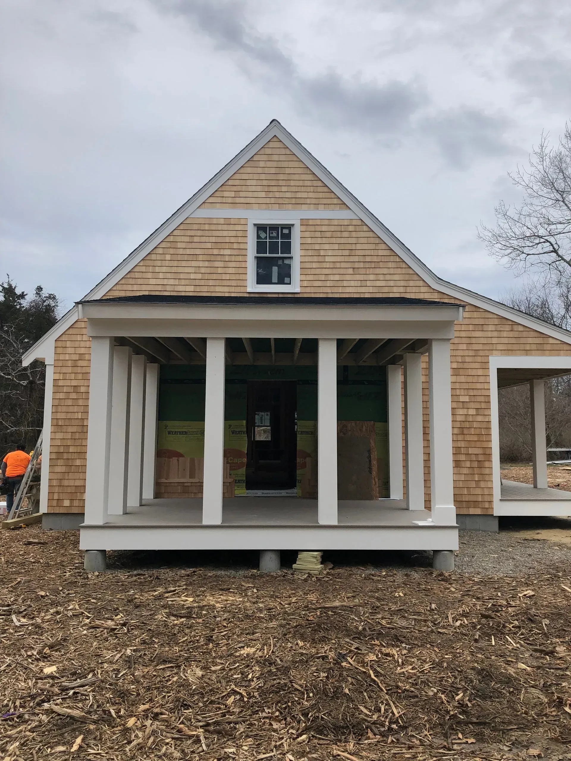 Small house under construction with porch and cedar siding.