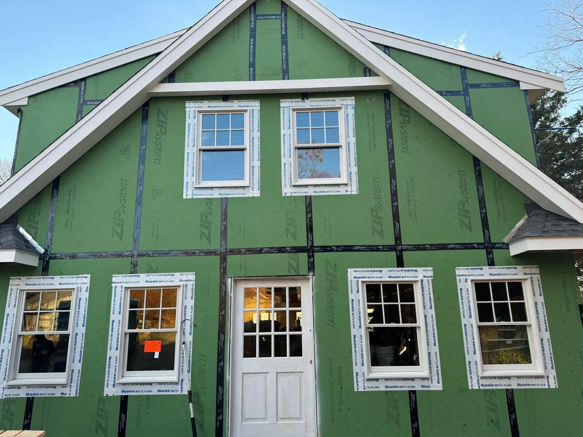 House exterior under construction, green sheathing, white trim and windows.