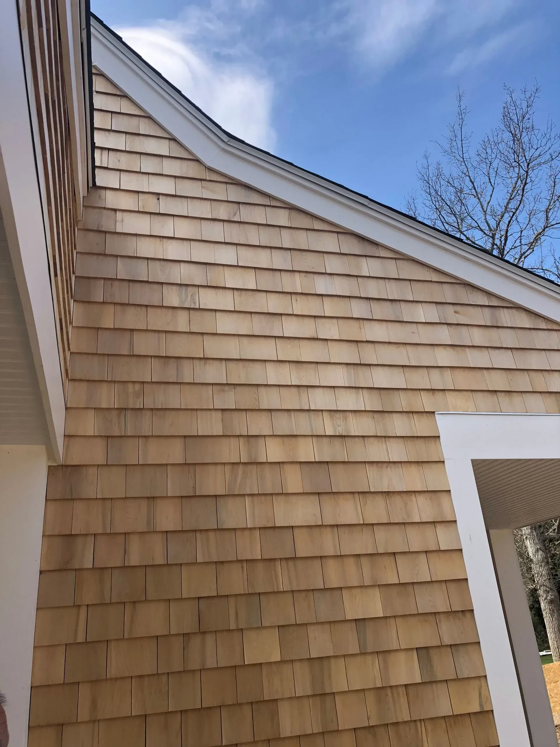 Cedar shake siding on a building exterior with white trim, against a blue sky.