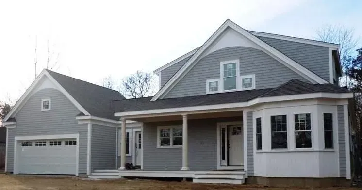 Gray two-story house with a detached garage and porch, on a sunny day.