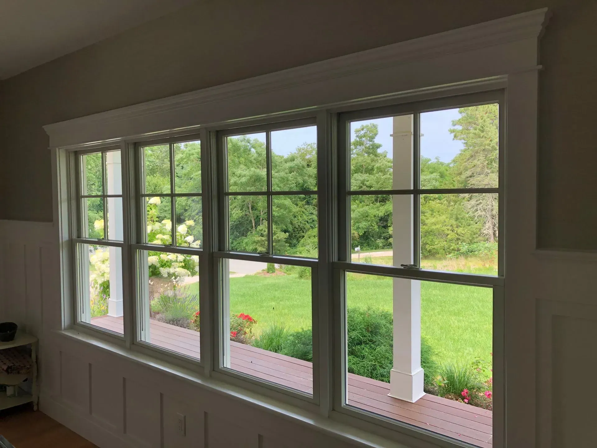 White-framed windows overlooking a green yard with trees and flowers, a white porch column is visible.