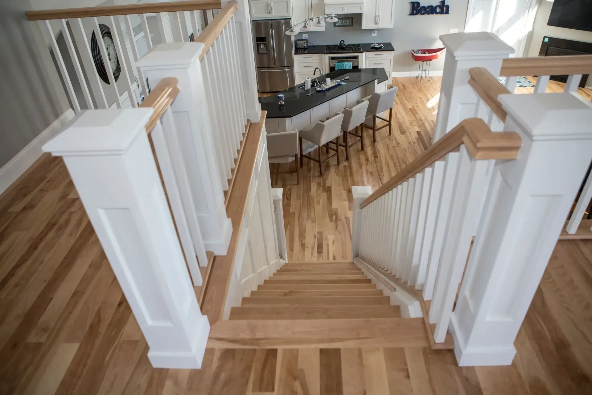 Staircase with white railing, light wood steps and flooring, leading to a kitchen with island and seating.